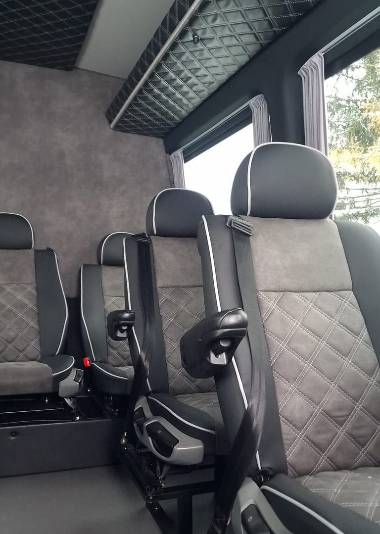 Widok wnętrza pojazdu z uwydatnieniem nowoczesnych foteli samochodowych z zagł&oacute;wkami i pasami bezpieczeństwa, z efektowną tapicerką przeszytą rombami.