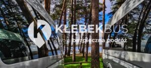 Odbicie tętniącego życiem lasu sosnowego i nieba na boku busa logo &bdquo;Kłębek Bus&rdquo; i napisem &bdquo;Twoja bezpieczna podr&oacute;ż&rdquo;