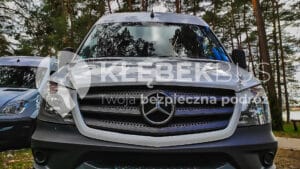 Widok z przodu busa Mercedes-Benz zaparkowanego na zewnątrz z drzewami w ruchliwym tle.