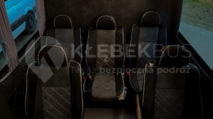 Wnętrze nowoczesnego busa z wygodnymi siedzeniami i pasami bezpieczeństwa, widziane z tylnego rzędu.