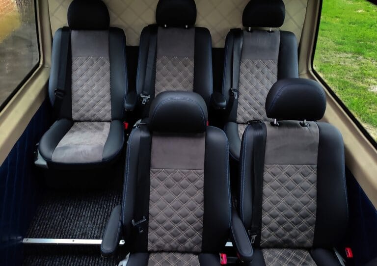 Wnętrze pojazdu przedstawiające trzy rzędy czystych i zajętych siedzeń pasażer&oacute;w z czarno-szarą tapicerką.