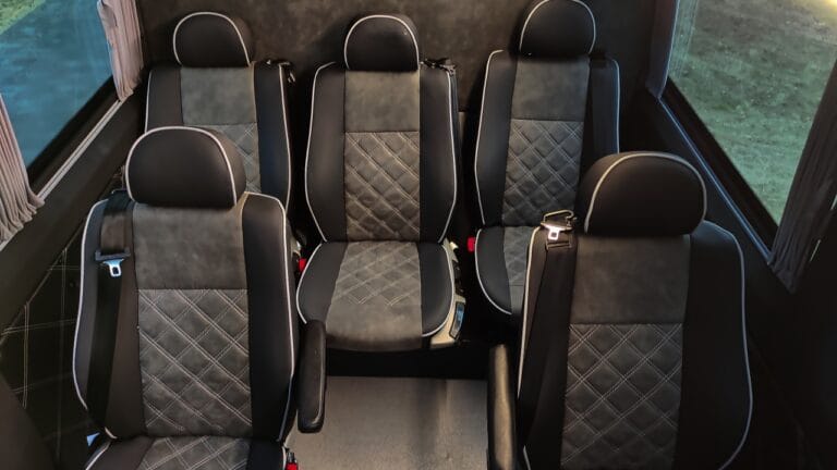 Wnętrze busa przedstawiające rząd czarnych tapicerowanych, wygodnych siedzeń