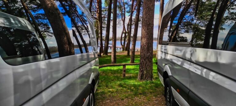 Dwa busy pasażerskie zaparkowane w lesie nad jeziorem